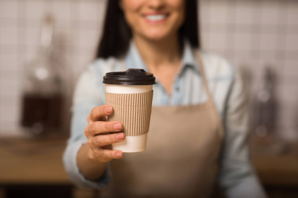 cropped shot of waitress holding coffee to go in paper cup with blurred background - Фото, зображення