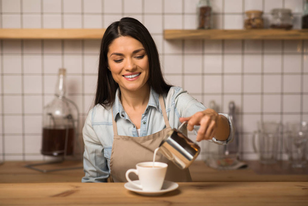 Portrait of smiling barista pouring milk into coffee - Zdjęcie, obraz