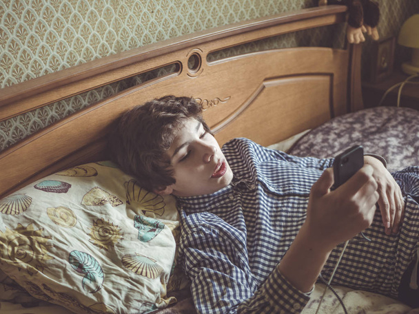 young teenager boy lying relaxing on the bed with phone - Photo, Image