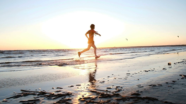 Ο άνθρωπος είναι εν ενεργεία τρέχει σε μια παραλία με φόντο kitesurfers στο ηλιοβασίλεμα, αργή κίνηση. - Πλάνα, βίντεο