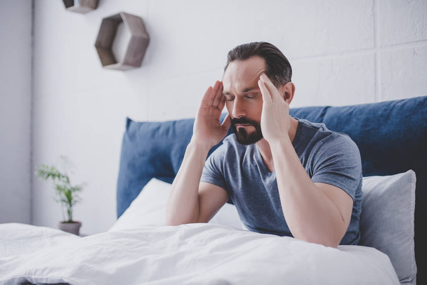caucasian bearded man with headache sitting on bed - Фото, зображення