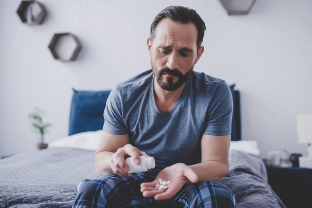 caucasian man spilling pills from container on the hand sitting on the bed - Photo, Image