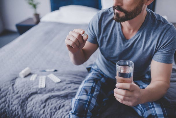 caucasian man holding pill and glass of water sitting on the bed - Foto, Imagem