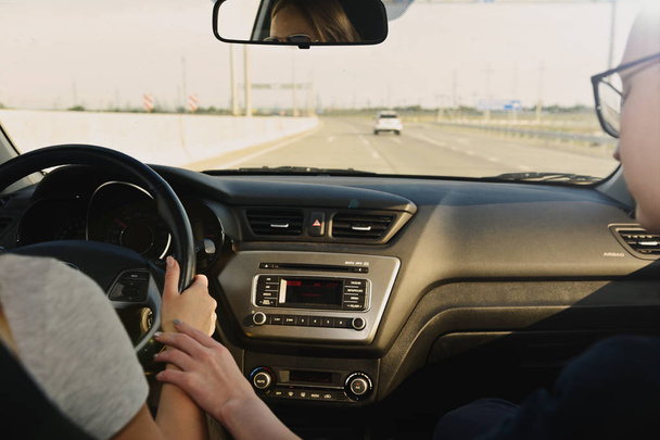 夕日に向かう途中車の前の席の女の子のカップル。彼女は運転が、彼女は彼女の手を保持しています。安全運転についてクローズ アップを撮影します。夕日を追え!恋人を旅行 - 写真・画像