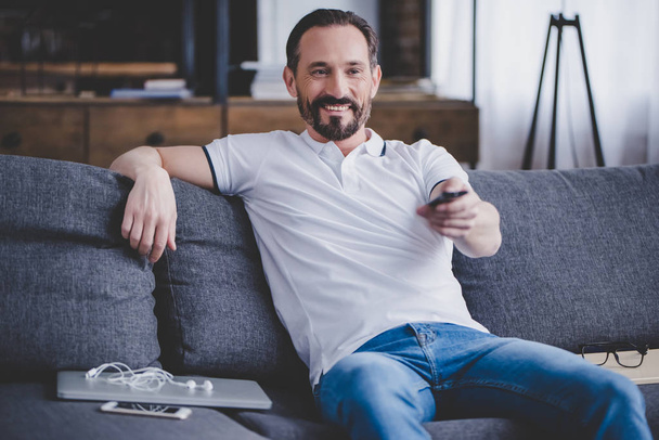 portrait of smiling bearded man watching tv at home on the sofa - Photo, image