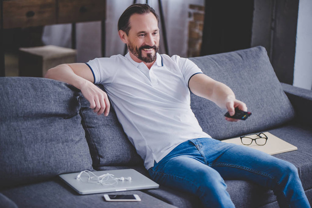 portrait of smiling bearded man watching tv at home on the sofa - Foto, Bild