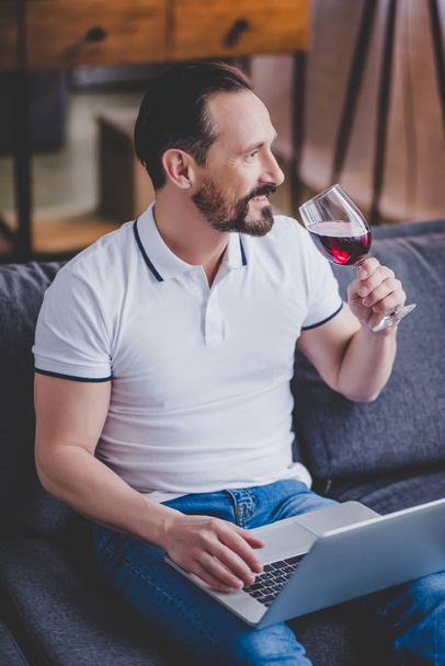 pohledný muž pomocí přenosného počítače doma a pít červené víno - Fotografie, Obrázek
