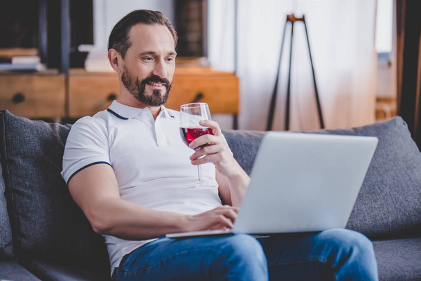 handsome man using laptop at home and drinking red wine - Фото, зображення