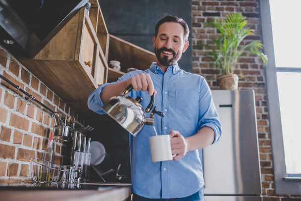 low angle view of happy man pouring coffee into the cup at morning in the kitchen - 写真・画像