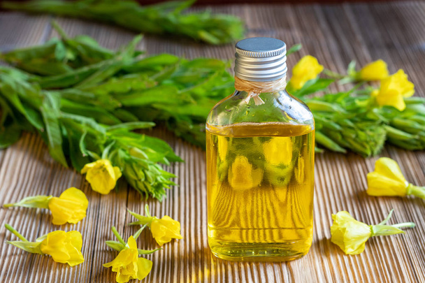 A bottle of evening primrose oil with fresh blooming plant in the background - Photo, Image