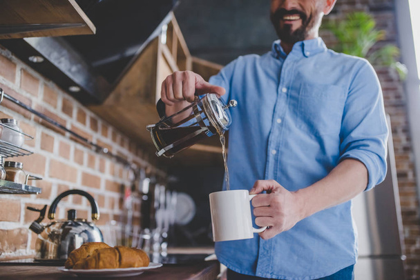 low angle view of happy man pouring coffee into the cup at morning in the kitchen - Zdjęcie, obraz