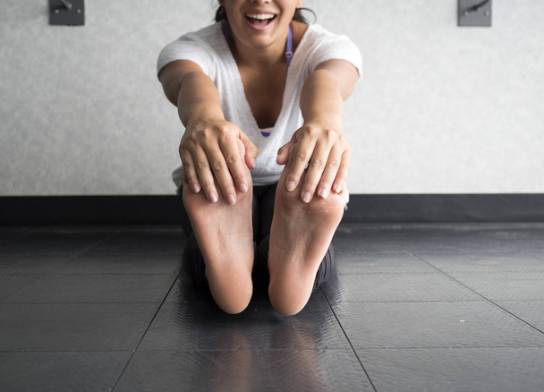Glimlachend actieve vrouw haar voeten te grijpen om te rekken van de hamstrings in de studio - Foto, afbeelding
