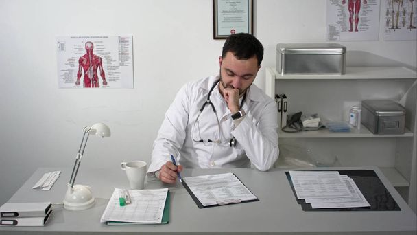 Thinking out loud. Thoughtful young bearded doctor in medical cabinet. - Zdjęcie, obraz