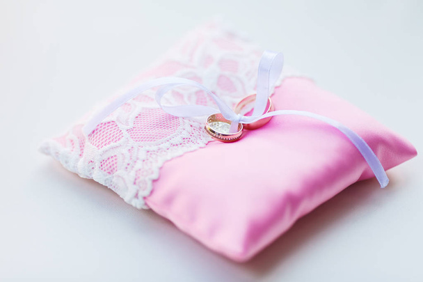 Anelli nuziali con diamanti si trovano in attesa del momento del matrimonio, sul piccolo cuscino cerimoniale rosa ricoperto di pizzo sottile
. - Foto, immagini