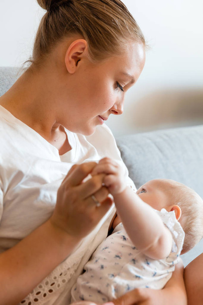 Zorgzame jonge moeder breastfeeds baby meisje thuis - Foto, afbeelding