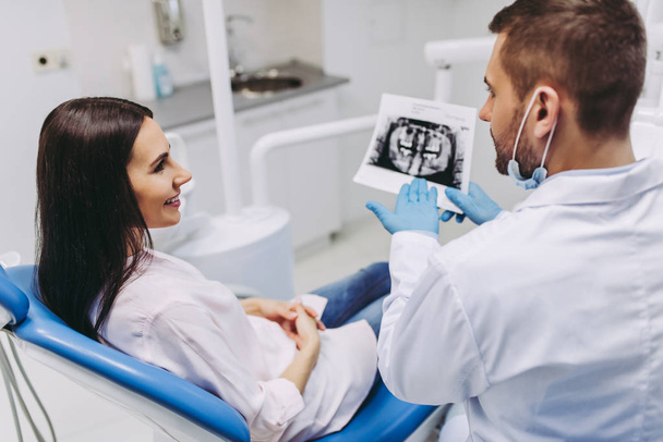 portrait of female patient talking with male dentist looking at x-ray in modern clinic - Photo, Image
