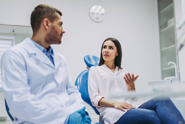 diş sandalye ve erkek diş hekimi diş kliniğinde konuşuyor bayan hasta - Fotoğraf, Görsel
