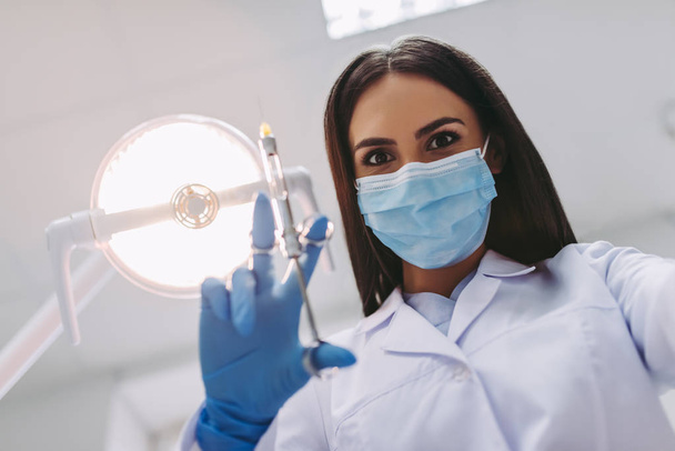 low angle view of dentist in medical mask holding syringe in modern dental clinic - Фото, изображение