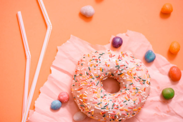 Sprinkled Pink Donut. Frosted sprinkled donut on pink background. Tubules for a cocktail. Broken colored candy. - Фото, изображение