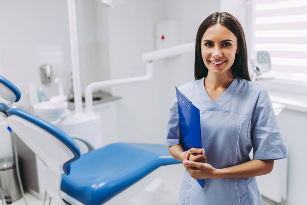 portrait of smiling female dentist with clipboard at working place in modern medical clinic - Foto, immagini