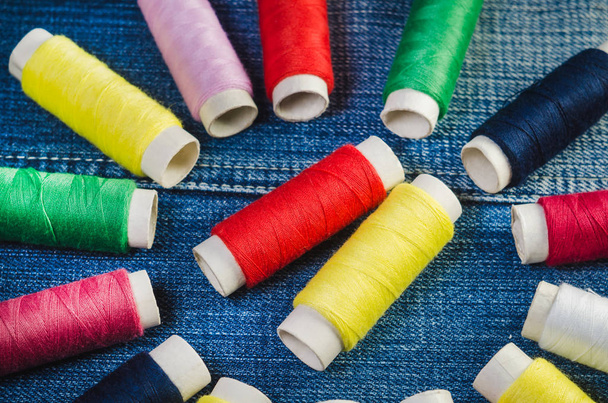 A circle of colored thread spools with a center of red and yellow thread spools on a denim - Photo, Image