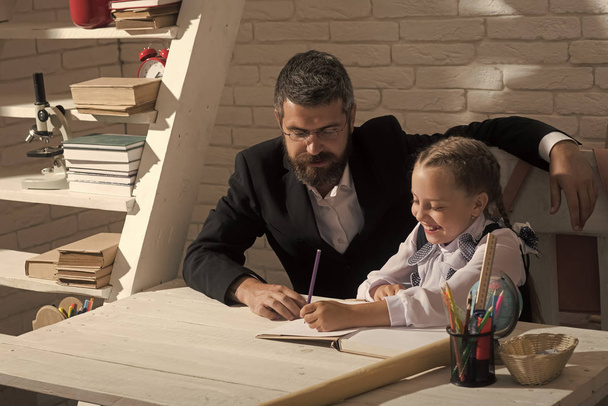 Home schooling. Kid and man sit by desk with school supplies - Foto, afbeelding