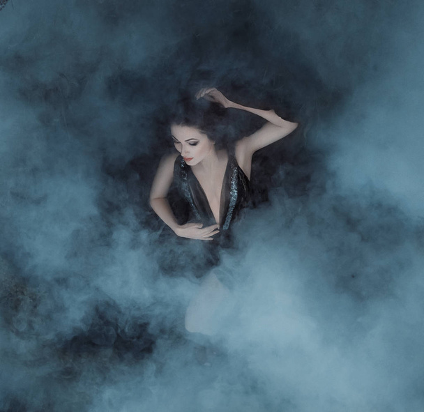 The dark vampire queen lies in the embrace of the fogs on her black dress with a deep neckline. The girl is enveloped in clouds of smoke, like blankets the clouds. Gothic atmosphere. Sleeping Beauty. - Fotoğraf, Görsel