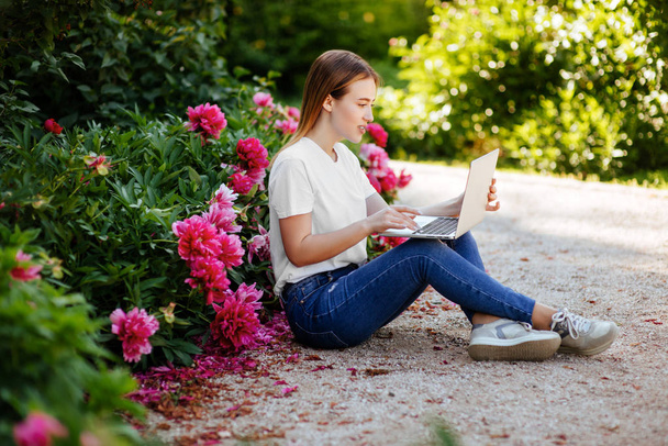 Closeup portrait of cheerful student girl lying down on purple floral park with laptop. - Fotoğraf, Görsel
