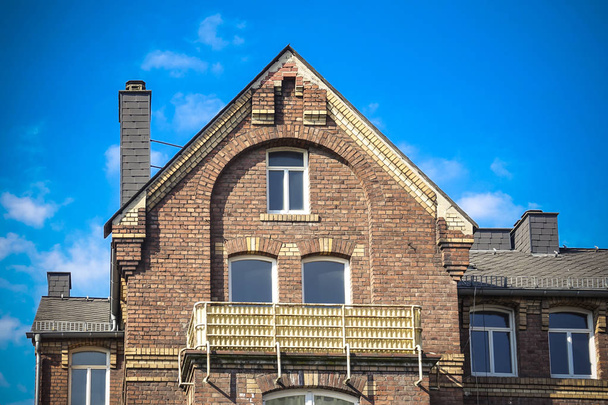 Facciata anteriore di un classico edificio in mattoni con balcone e dettaglio ad arco sopra le finestre contro un cielo limpido e soleggiato
 - Foto, immagini