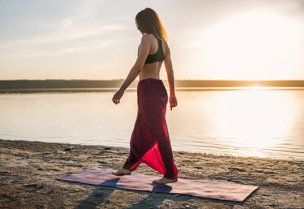 Yoga vrouw op het strand bij zonsondergang. - Foto, afbeelding