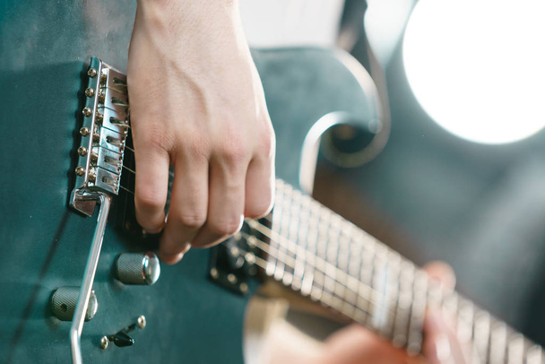 Primer plano del hombre tocando en la guitarra eléctrica durante el concierto o en el estudio de música. Instrumentos musicales, pasión y concepto de hobby. - Foto, imagen