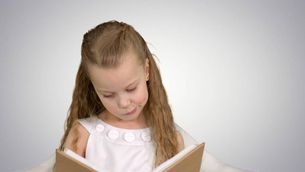 Pretty little girl sitting with book and reading on white background - Foto, imagen