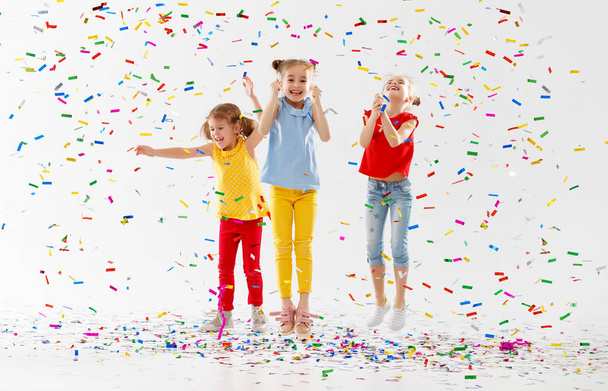 niños felices en vacaciones divertirse y saltar en confeti multicolor sobre fondo blanco
 - Foto, imagen
