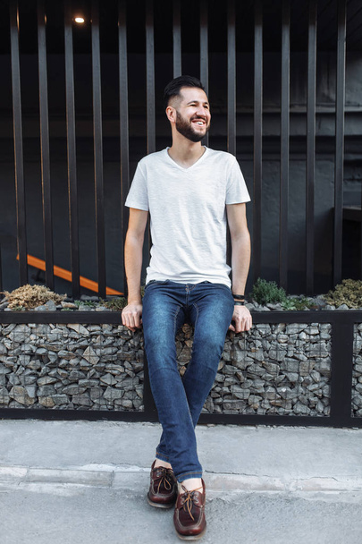 stylish hipster man in white blank t-shirt, on black fence background - 写真・画像