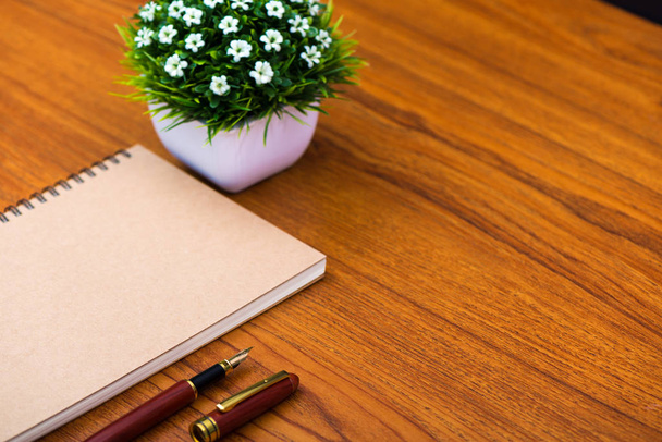 Fountain pen or ink pen with notebook paper and little decoration tree in white vase on wooden working table with copy space, office desk concept idea. - 写真・画像