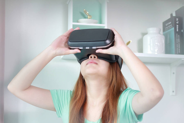 Young woman wearing virtual reality glasses at home. A virtual reality headset is a head-mounted device that provides virtual reality for the wearer. - Photo, Image