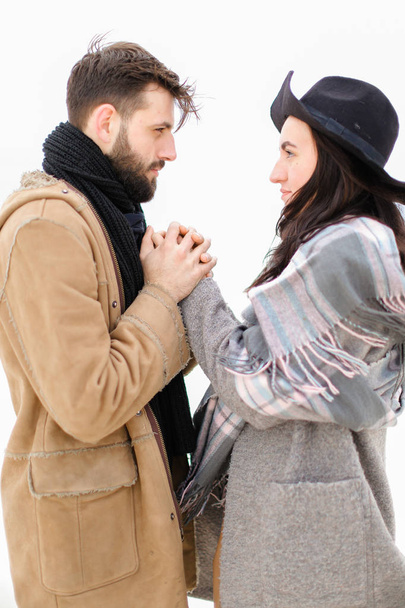 Portrait of young european man holding woman hand in white background, wearing coat with scarf. - Photo, image
