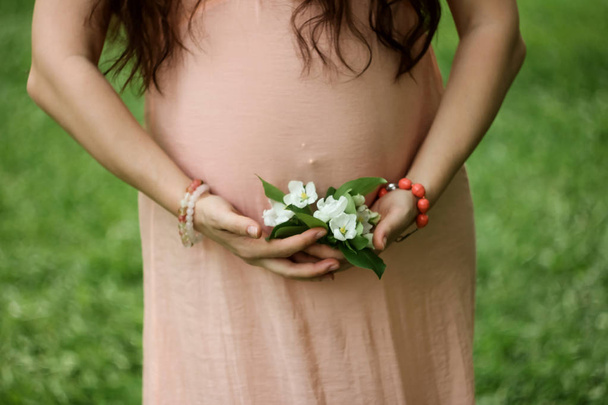 schwangere Frau mit dunklen Haaren in rosa mit weißen Blumen auf grünem Gras Hintergrund - Foto, Bild