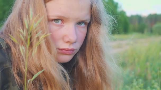 Portrait of sad blonde girl 11 years old. Pensively and dreamily looks at the blade of grass. - Filmagem, Vídeo