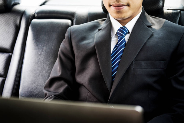 Csinos fiatal üzletember használ laptop, és ül hátul autó ülés - Fotó, kép