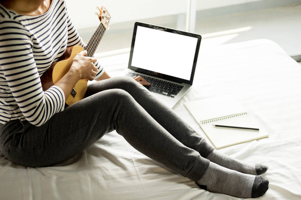 heureux jeune asiatique femme jouer ukulele assis sur lit dans chambre
 - Photo, image