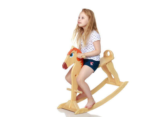 Dziewczyna, kołysanie na drewnianym koniu. - Zdjęcie, obraz