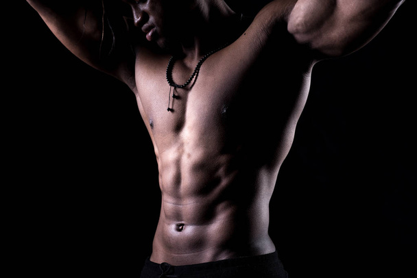 Tiro cortado de um homem sem camisa no estúdio. Modelo masculino africano com musculação sobre fundo preto
 - Foto, Imagem
