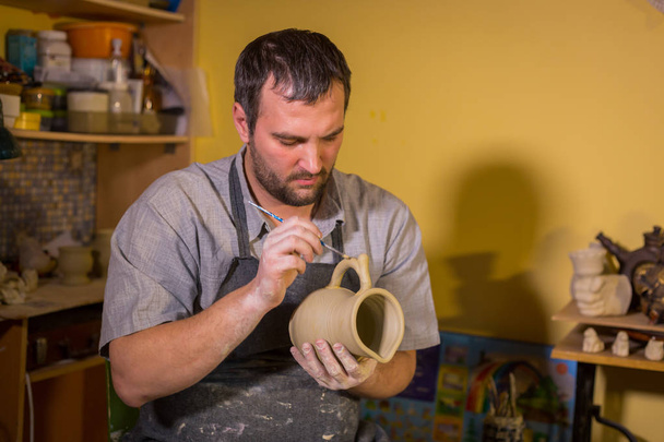 Professional male potter working in workshop, studio - putting handle on ceramic mug. Handmade, small business, crafting work concept - Zdjęcie, obraz