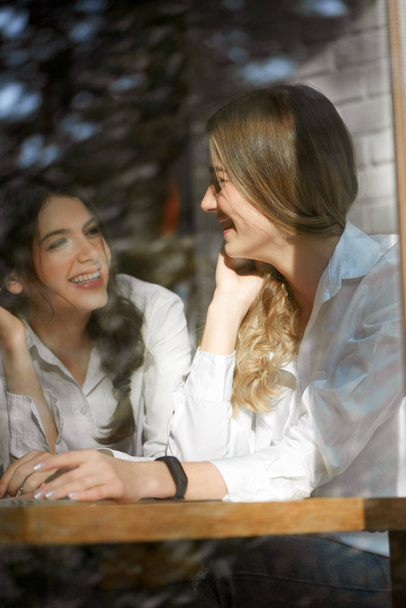 Two female friends laughing near window glass. - Фото, зображення