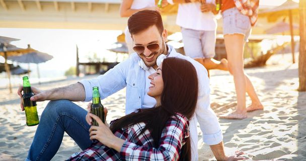 Feliz joven pareja sonriendo y bebiendo cerveza en la playa - Foto, imagen