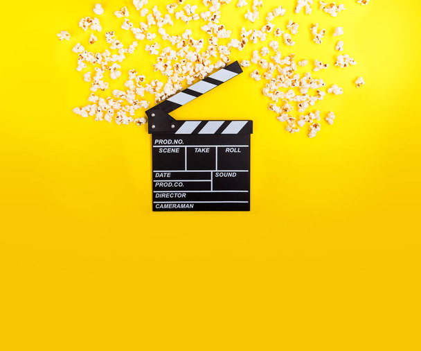 Cinema background. Film watching. Popcorn and clapperboard on yellow background top view copy space - Foto, Imagen