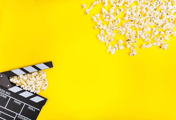 Cinema background. Film watching. Popcorn and clapperboard on yellow background top view copy space - Photo, Image