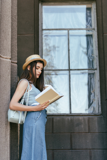 side view of beautiful girl in hat holding paper cup and reading book - Foto, Imagem