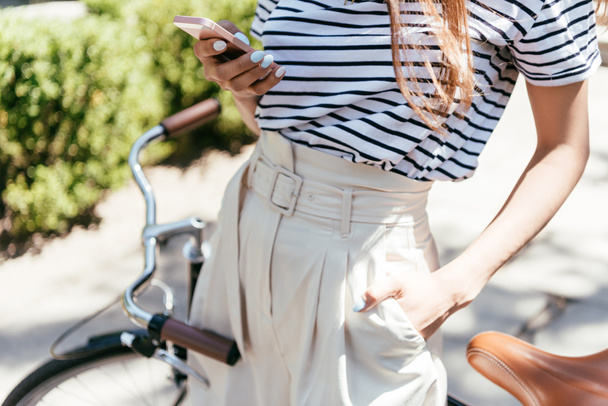 cropped shot of girl using smartphone while standing with bicycle on street - Photo, Image